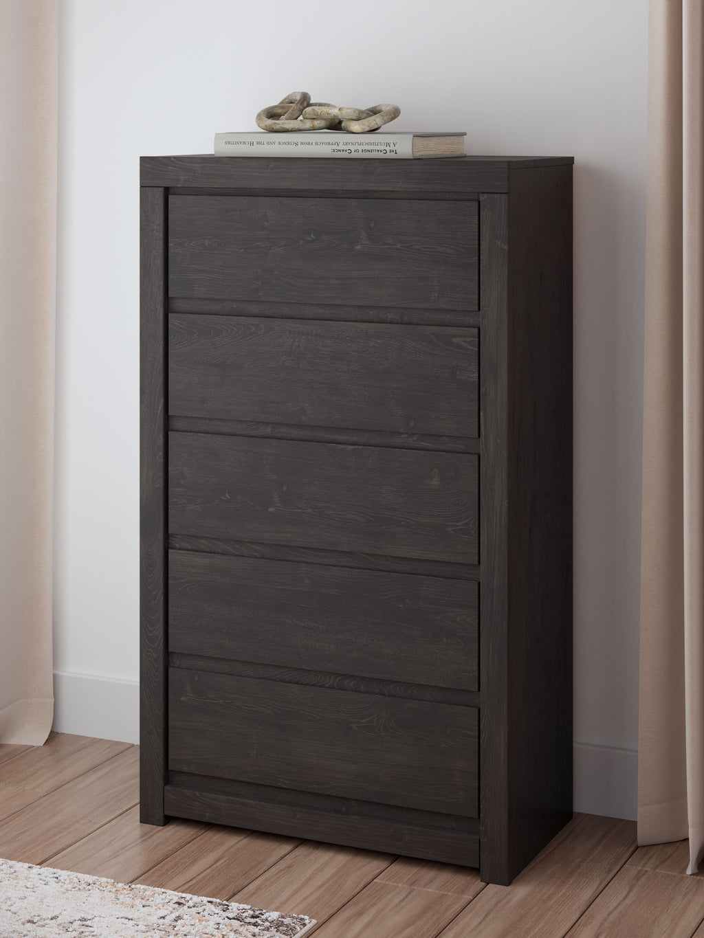 Charcoal five-drawer chest in a room, with textured drawer fronts and top surface