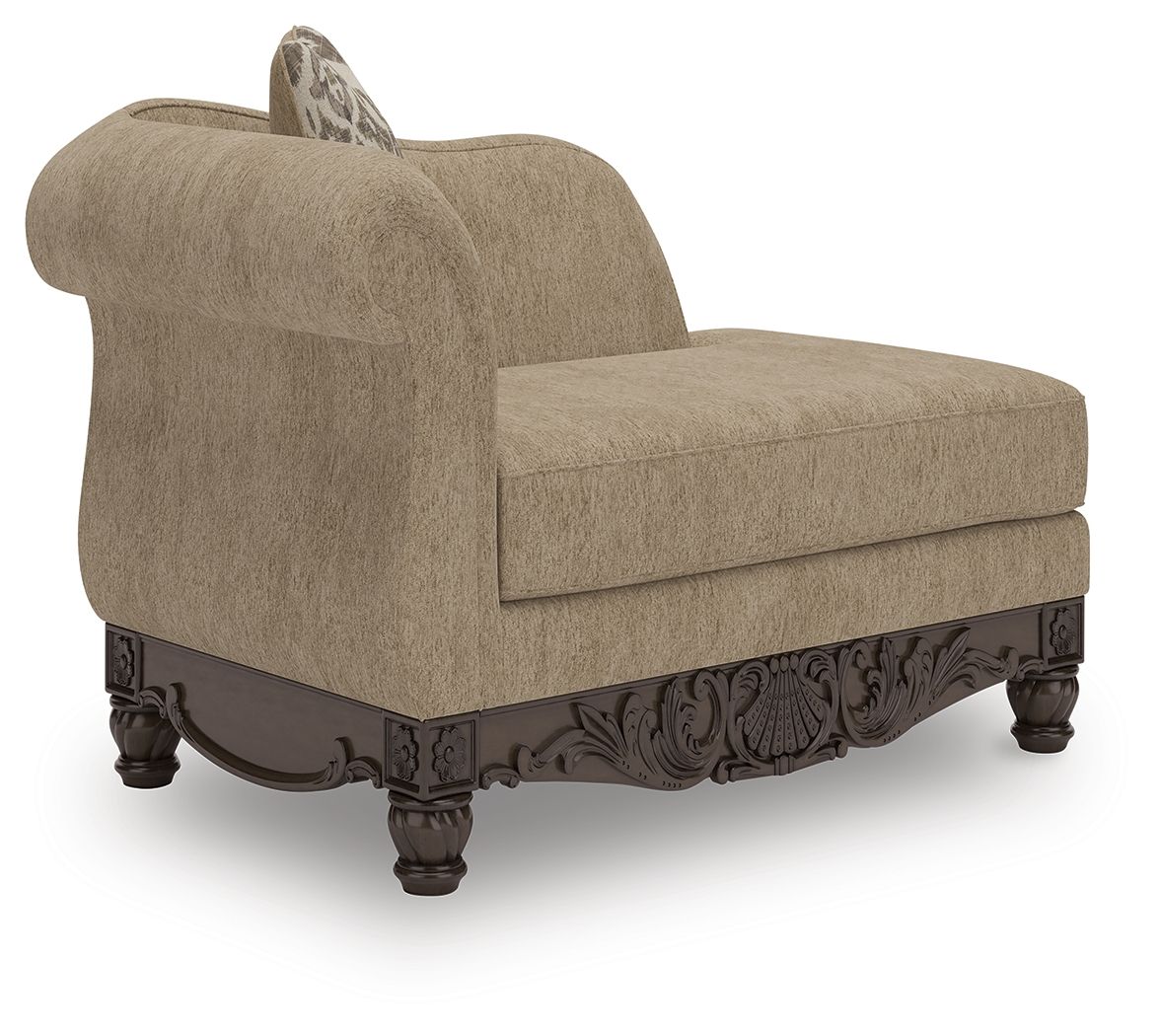 Beige corner chaise with patterned pillow and dark carved wooden base, side view.