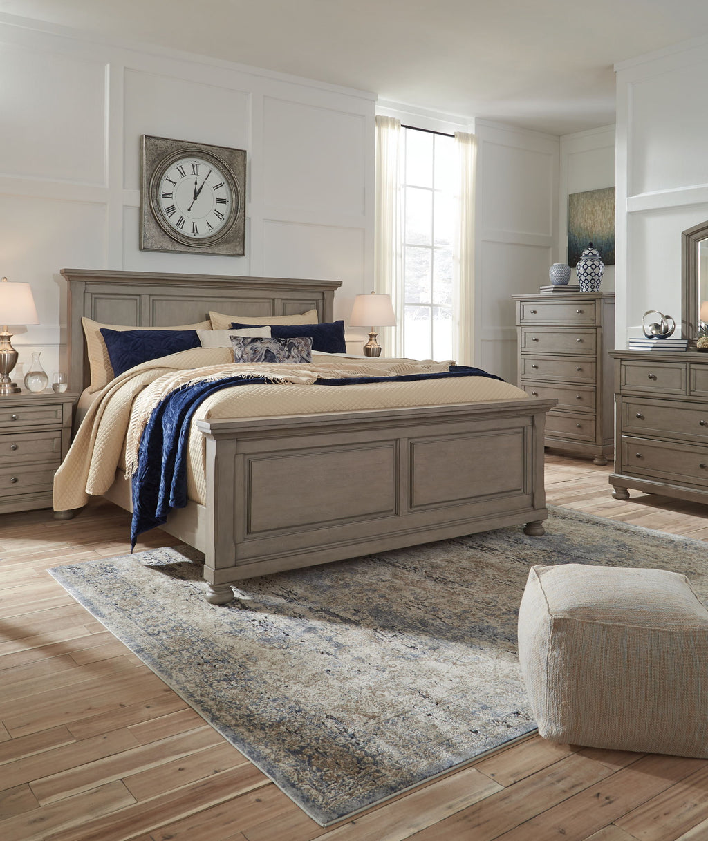 Gray panel bed centered in room with cream quilt, navy cover, and patterned pillows