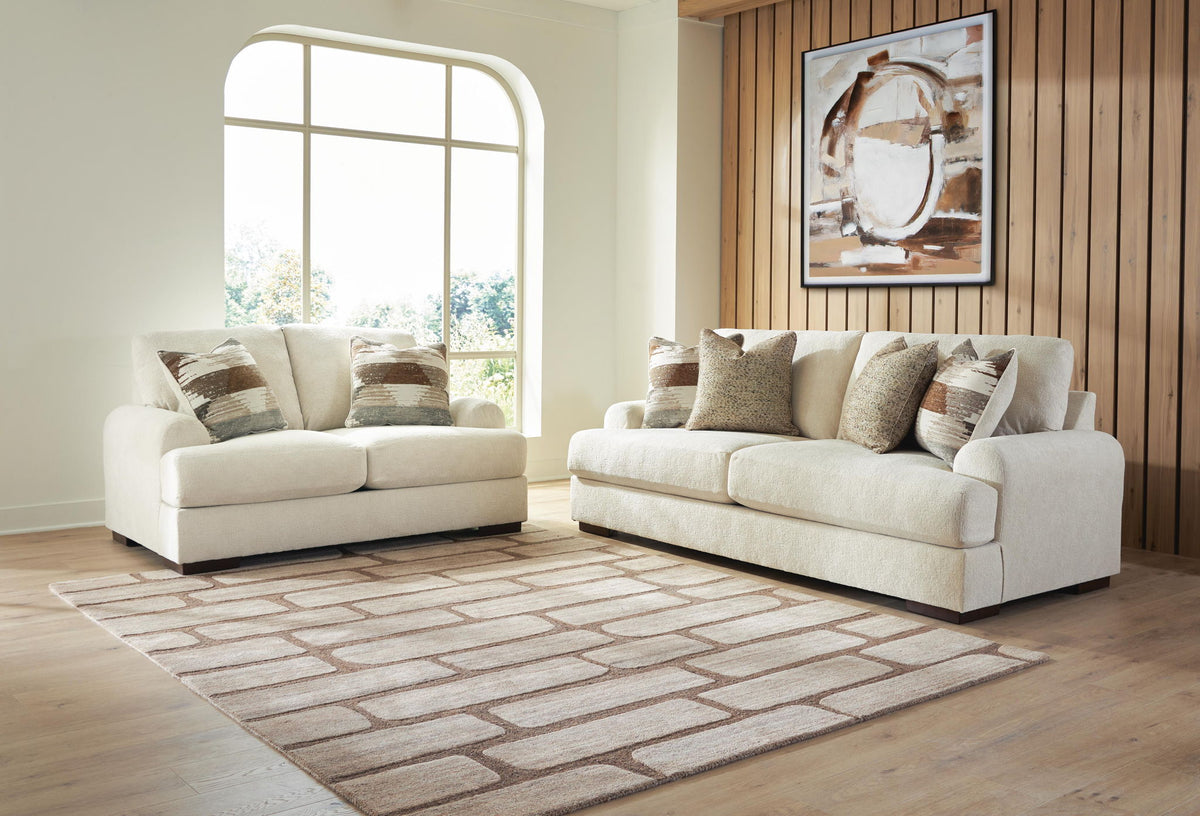 Beige sofa and loveseat set with patterned throw pillows in a living room