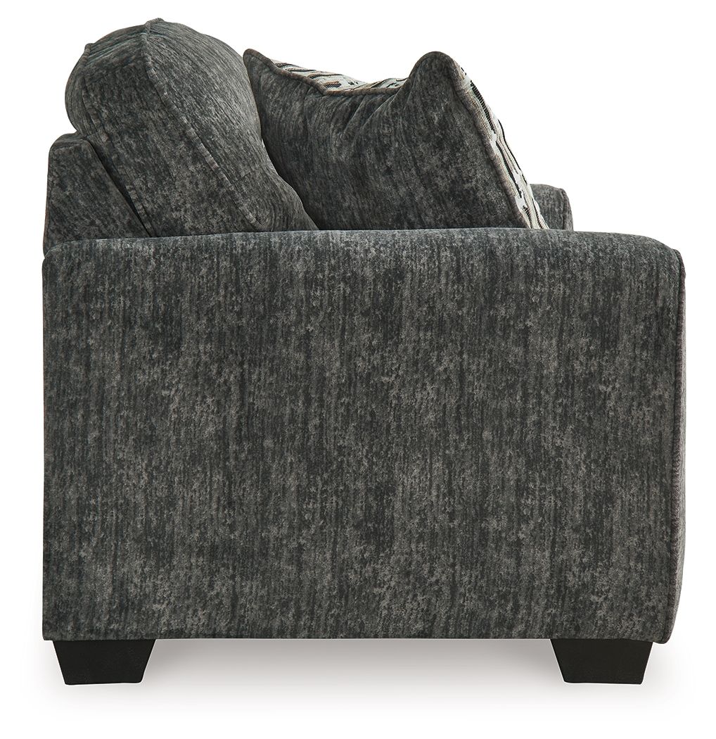 Gunmetal gray loveseat close-up with textured fabric, armrest, and patterned pillow