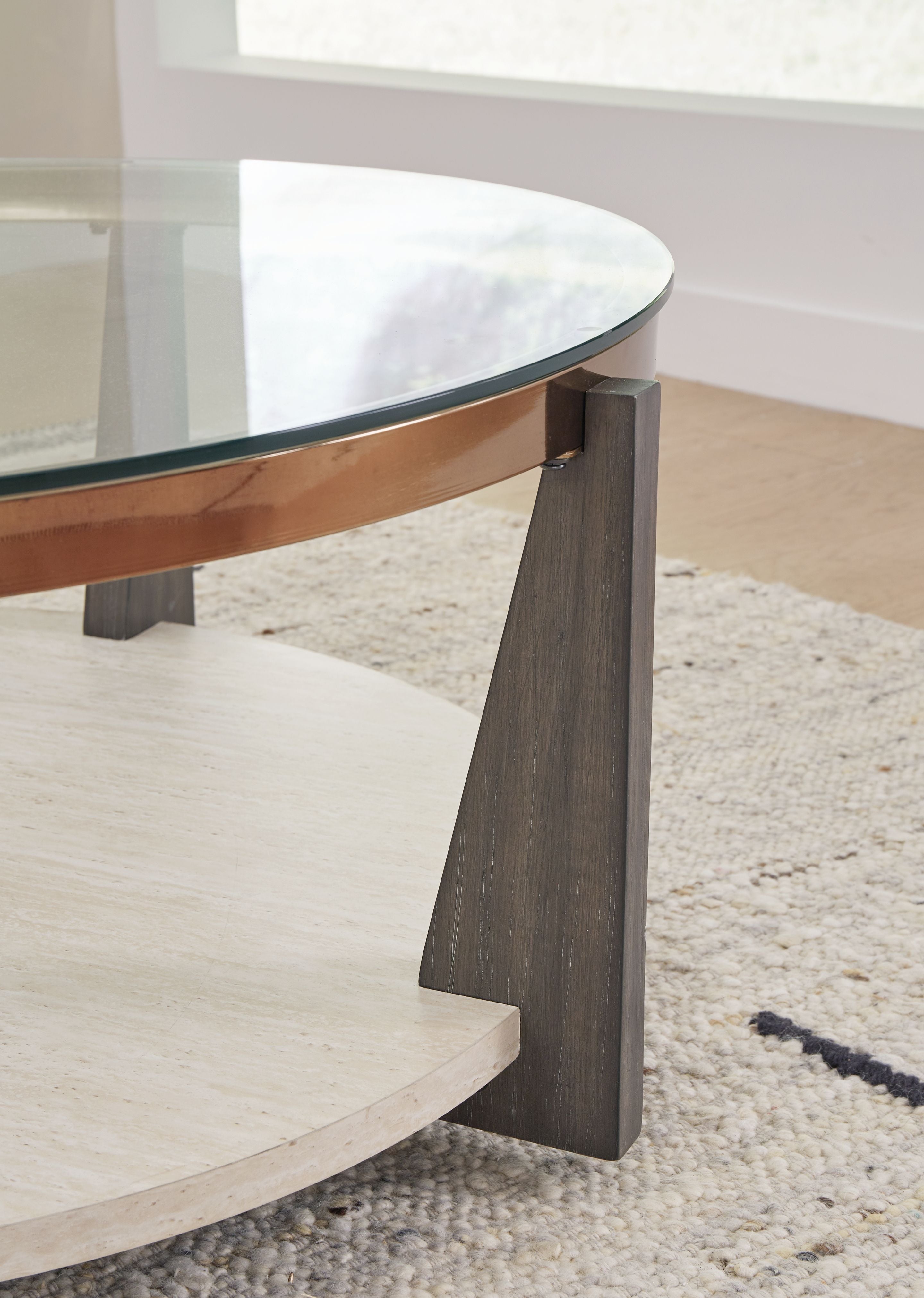 Round cocktail table corner detail with glass top, dark leg, and wood-tone rim