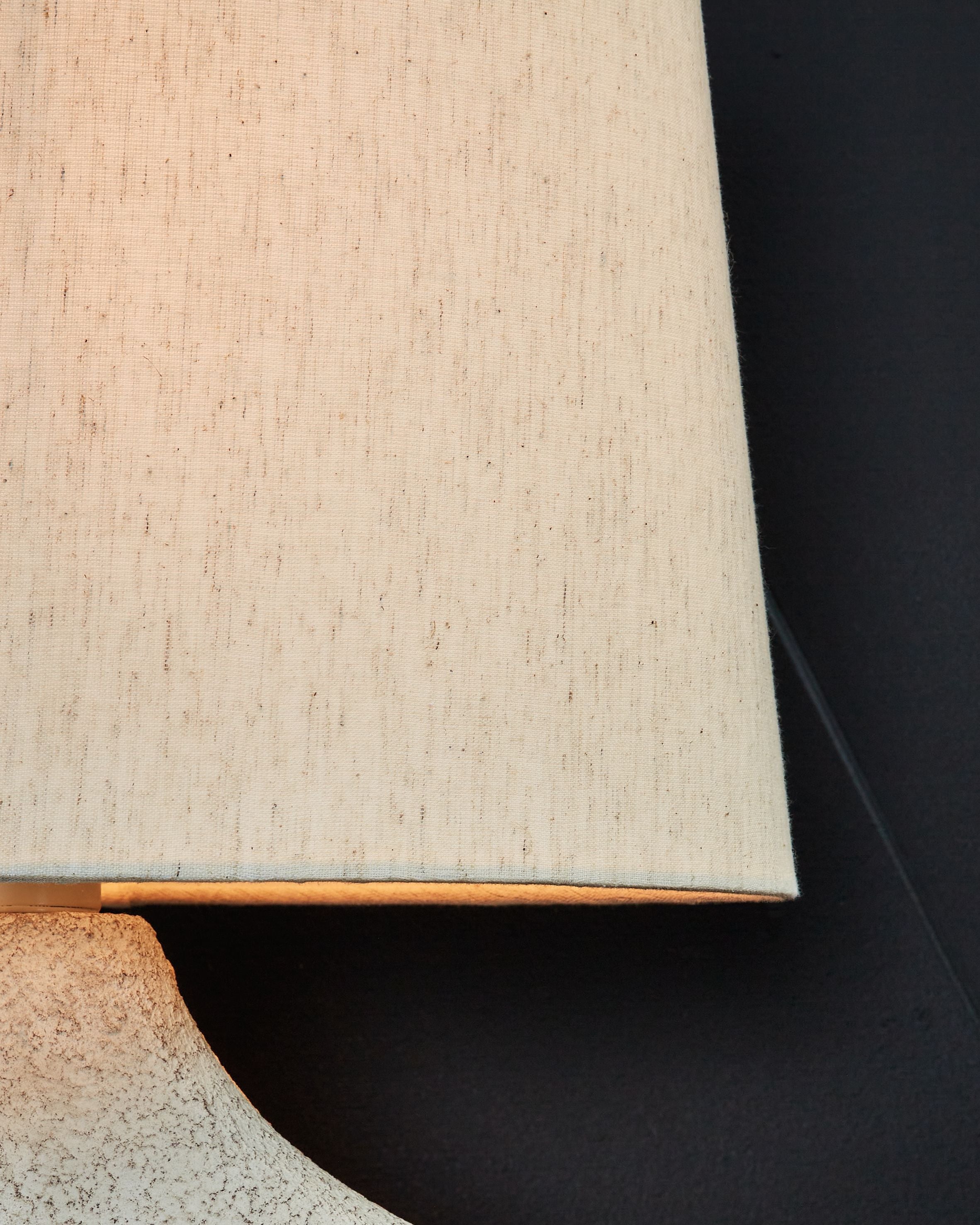 Paper table lamp close-up: square fabric shade edge over textured antique beige base