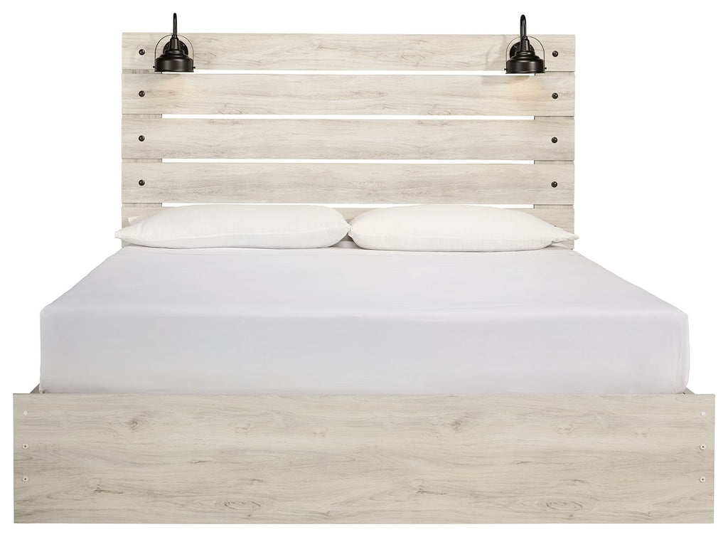 Light wood panel bed with two lamps on headboard; white bedding and closed drawers below