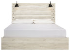 Light wood panel bed with two lamps on headboard; white bedding and closed drawers below