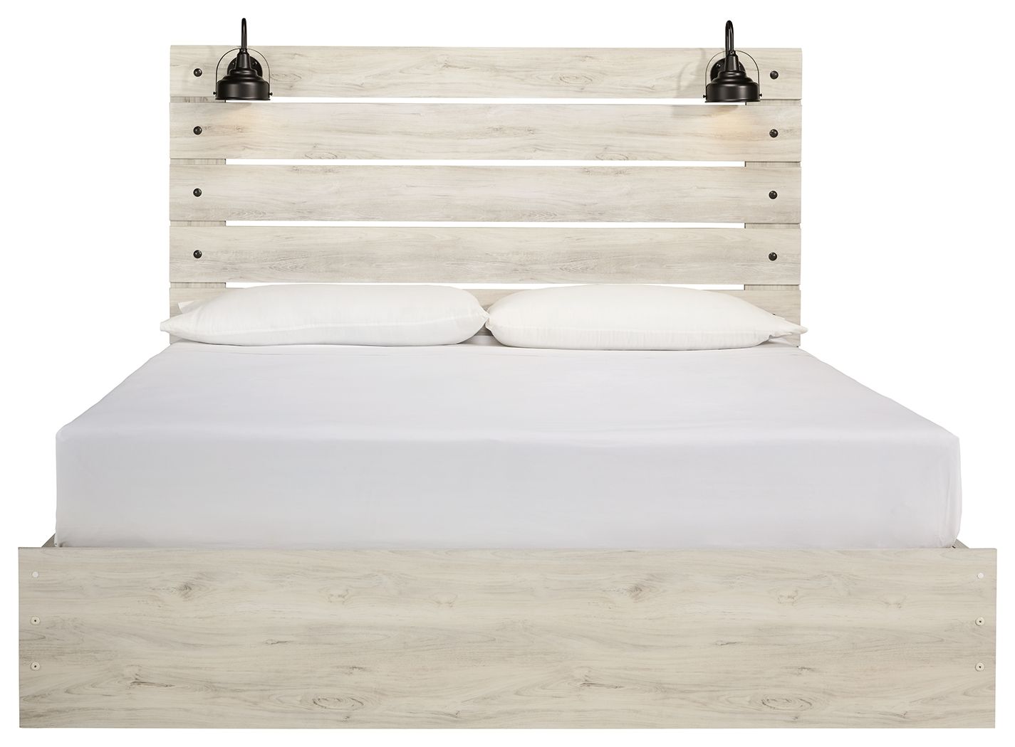 Light wood panel bed with two lamps on headboard; white bedding and closed drawers below