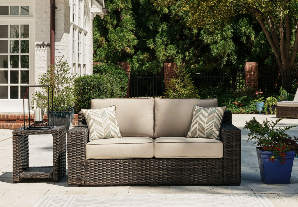 Brown wicker loveseat with beige cushions and two chevron-pattern pillows