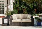 Brown wicker loveseat with beige cushions and two chevron-pattern pillows