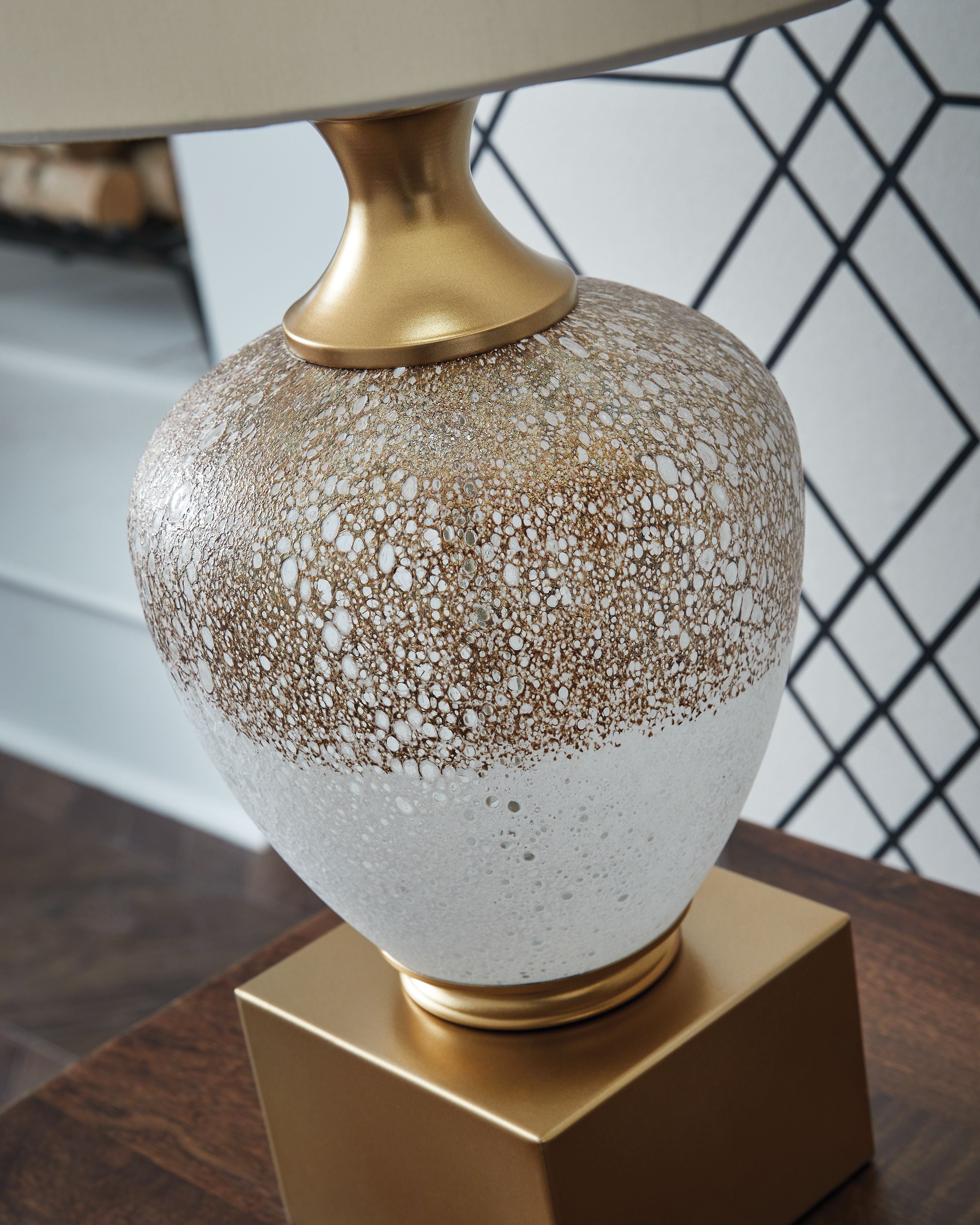 Glass table lamp close-up, gold neck and speckled white-brown glass body.