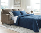 Sofa sleeper opened into a bed with blue comforter and cream accent bedding on taupe upholstery