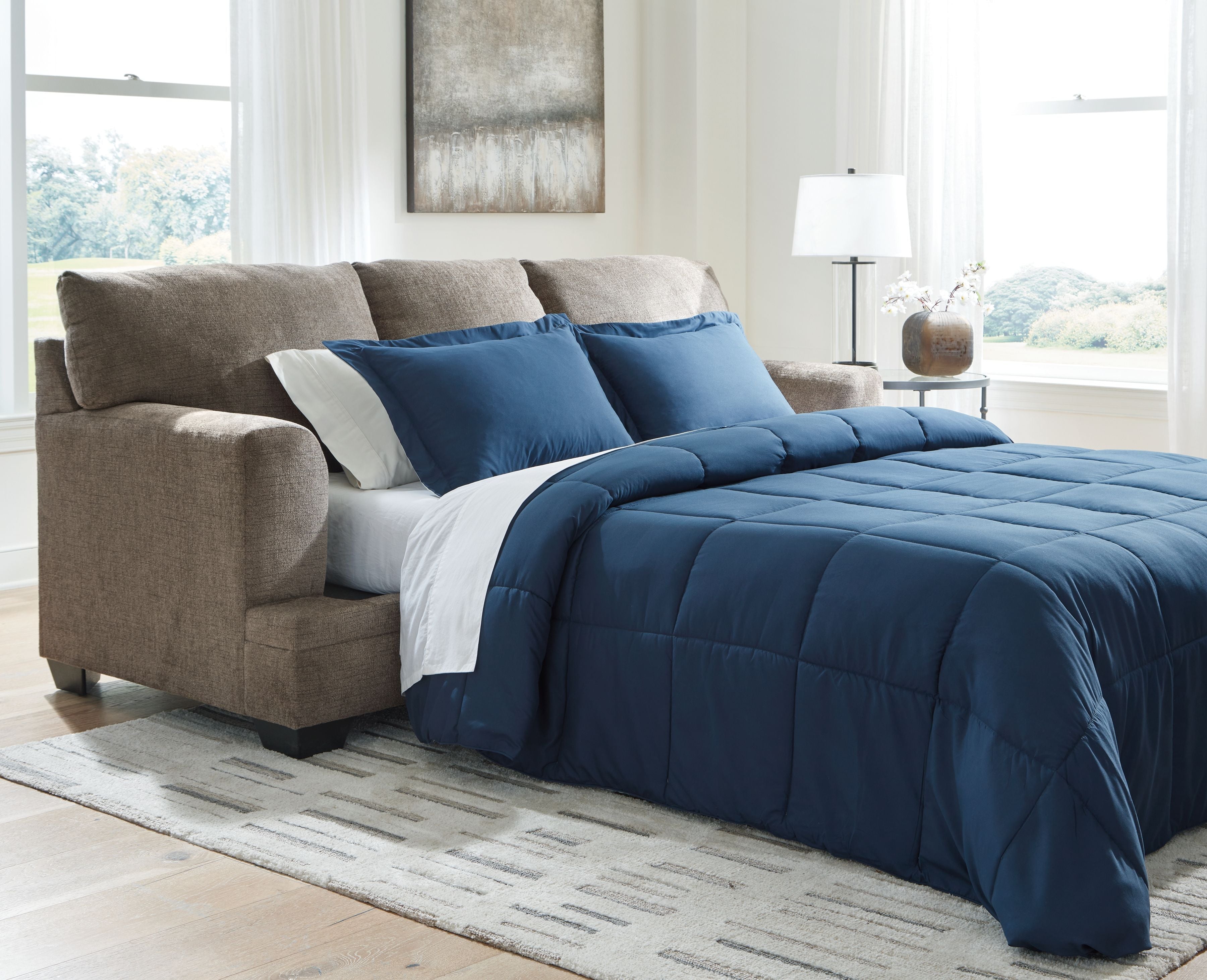 Sofa sleeper opened into a bed with blue comforter and cream accent bedding on taupe upholstery