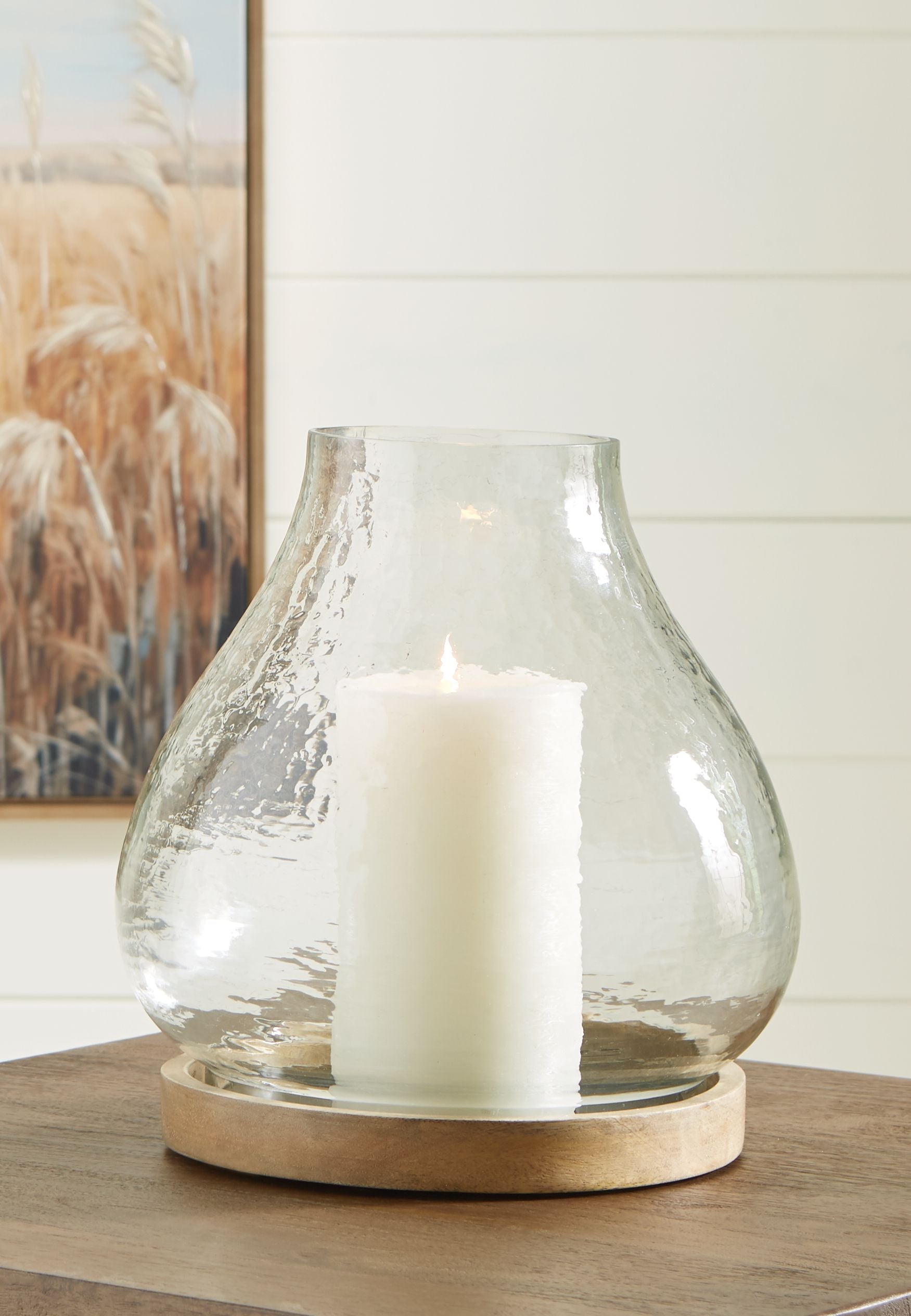 Clear glass vase candle holder with white candle on round wooden base