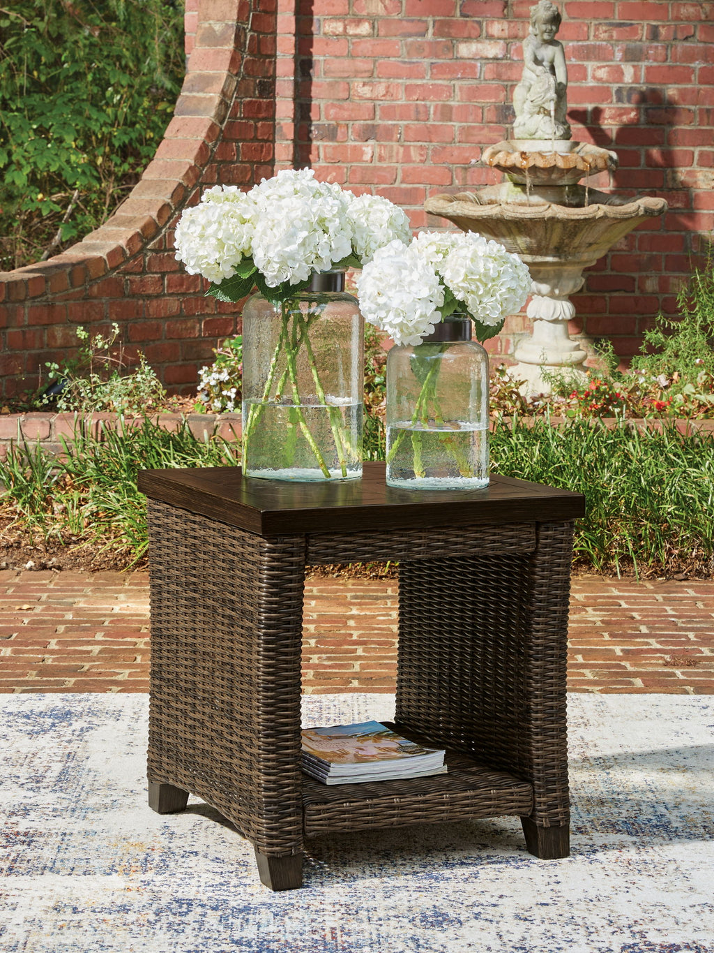 Rectangular outdoor side table with dark brown top and woven base, open lower shelf