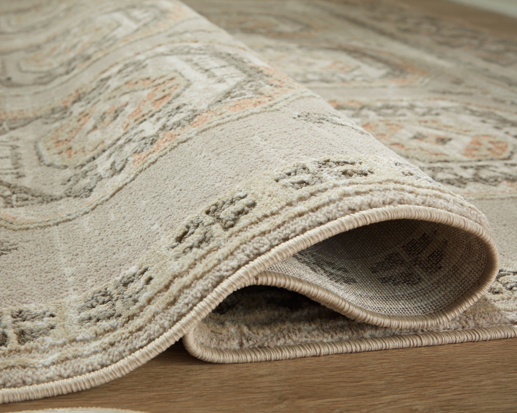 Beige rug with textured pile and woven edge border, rolled corner detail