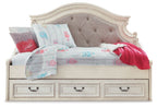 Chipped white twin day bed with tufted gray headboard, patterned quilt, red throw, pillows