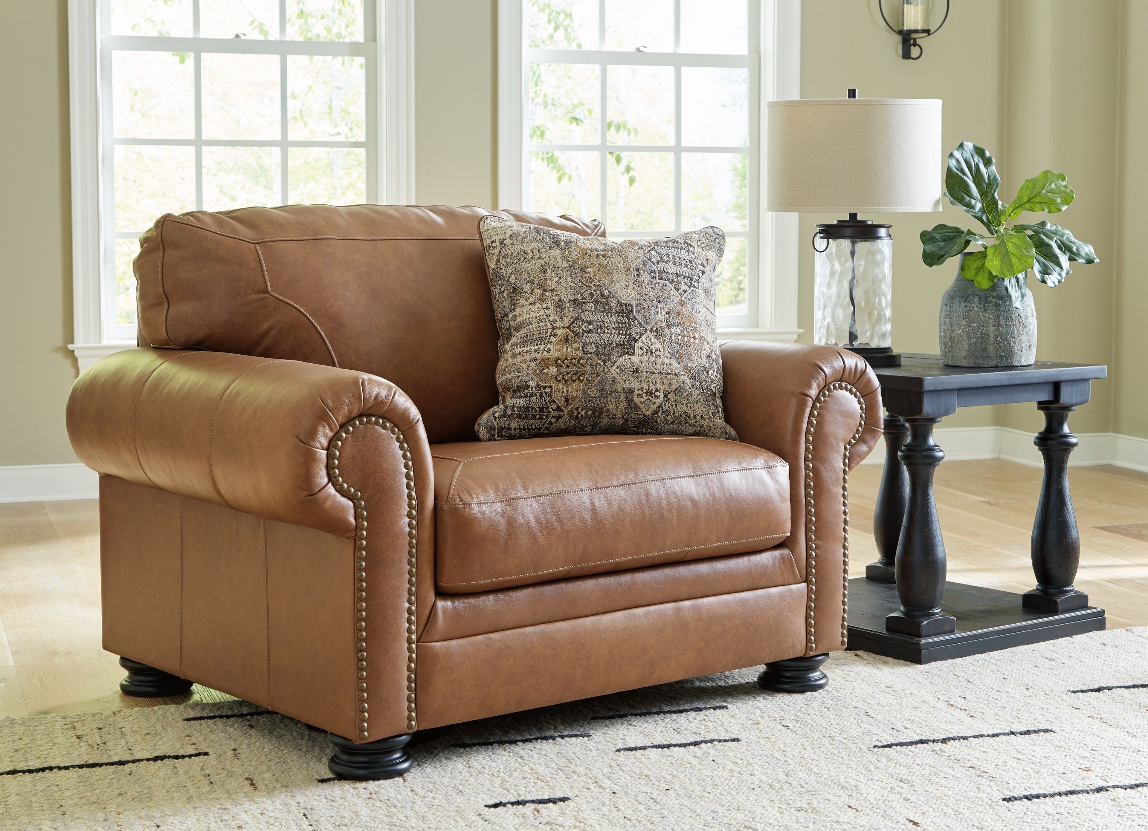 Caramel chair and a half with nailhead trim, patterned pillow, and dark tapered legs