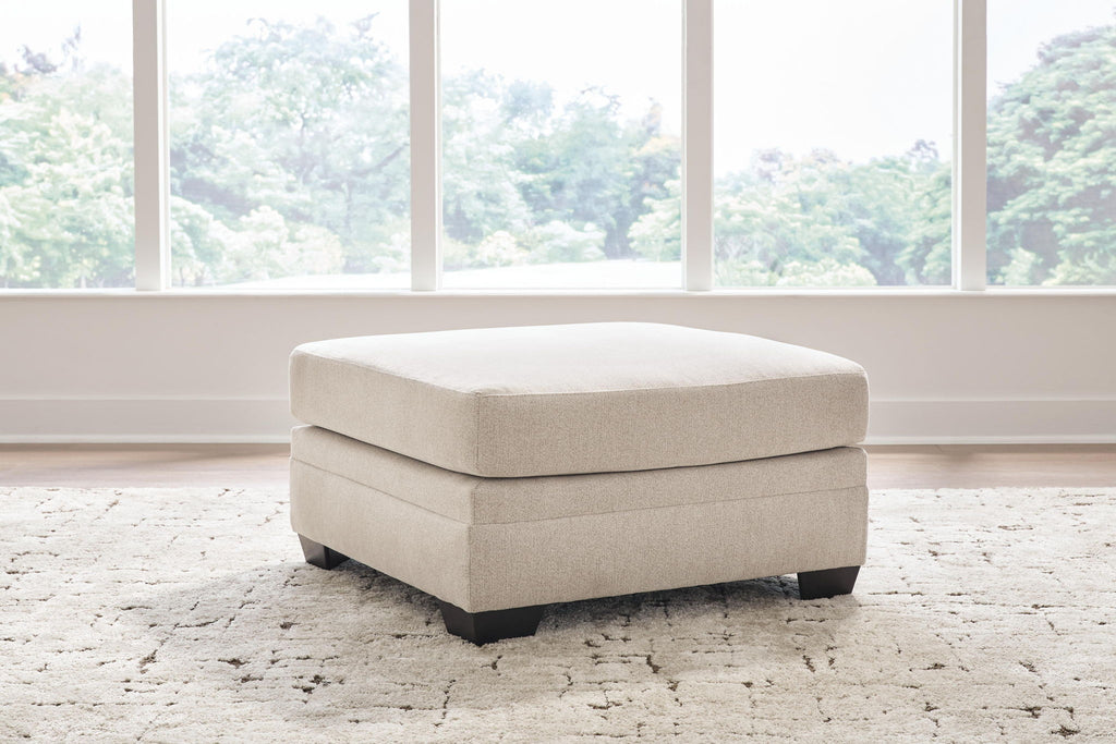 Beige square upholstered ottoman with thick seat cushion and dark legs