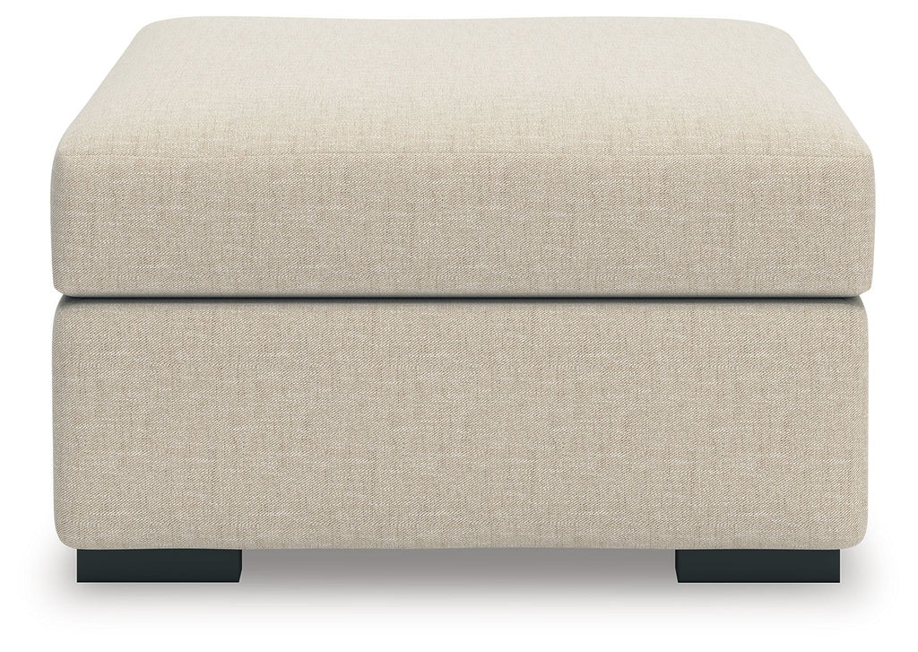Light beige upholstered ottoman with thick padded top and black block feet