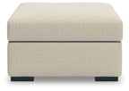 Light beige upholstered ottoman with thick padded top and black block feet