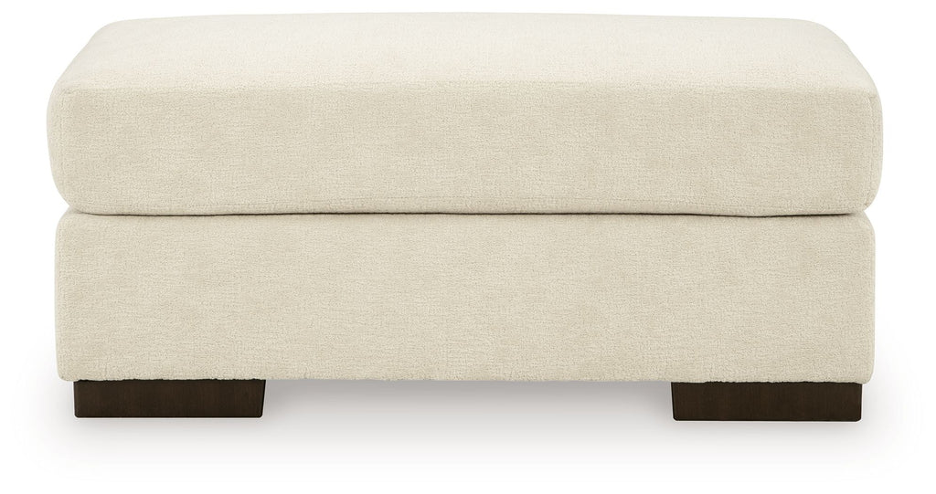 Beige fabric ottoman with padded top and dark legs.