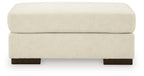 Beige fabric ottoman with padded top and dark legs.
