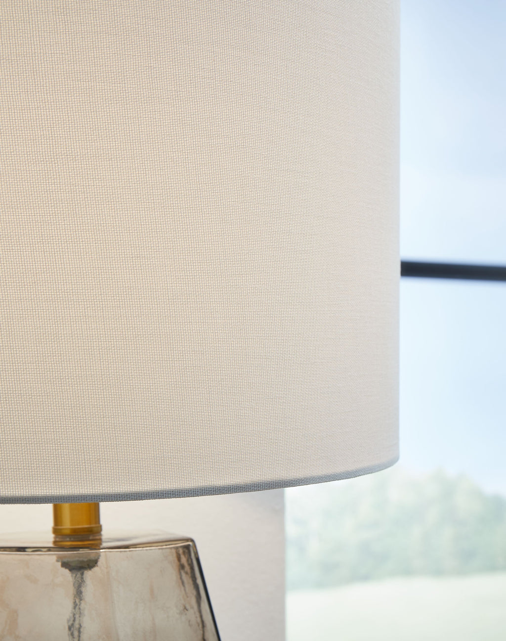 White drum lamp shade over gray glass base with gold stem