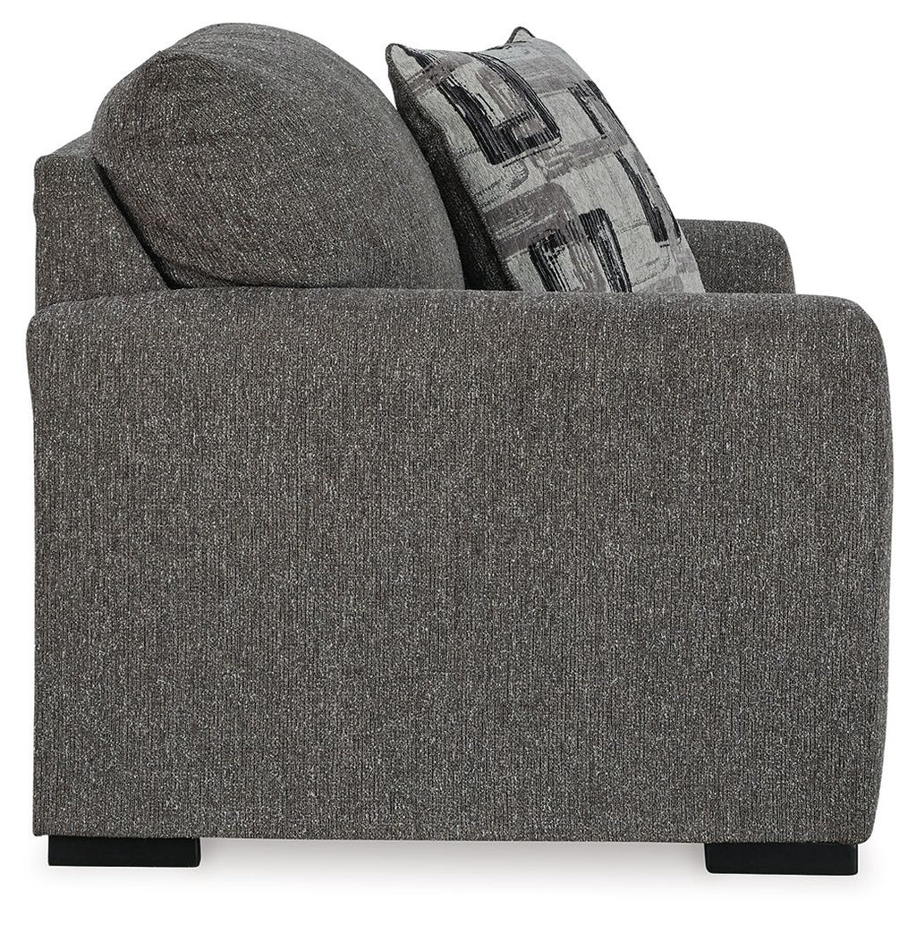 Gray chair and a half from front-left with patterned throw pillow and wide padded arms