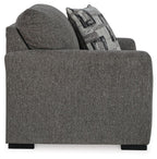 Gray chair and a half from front-left with patterned throw pillow and wide padded arms