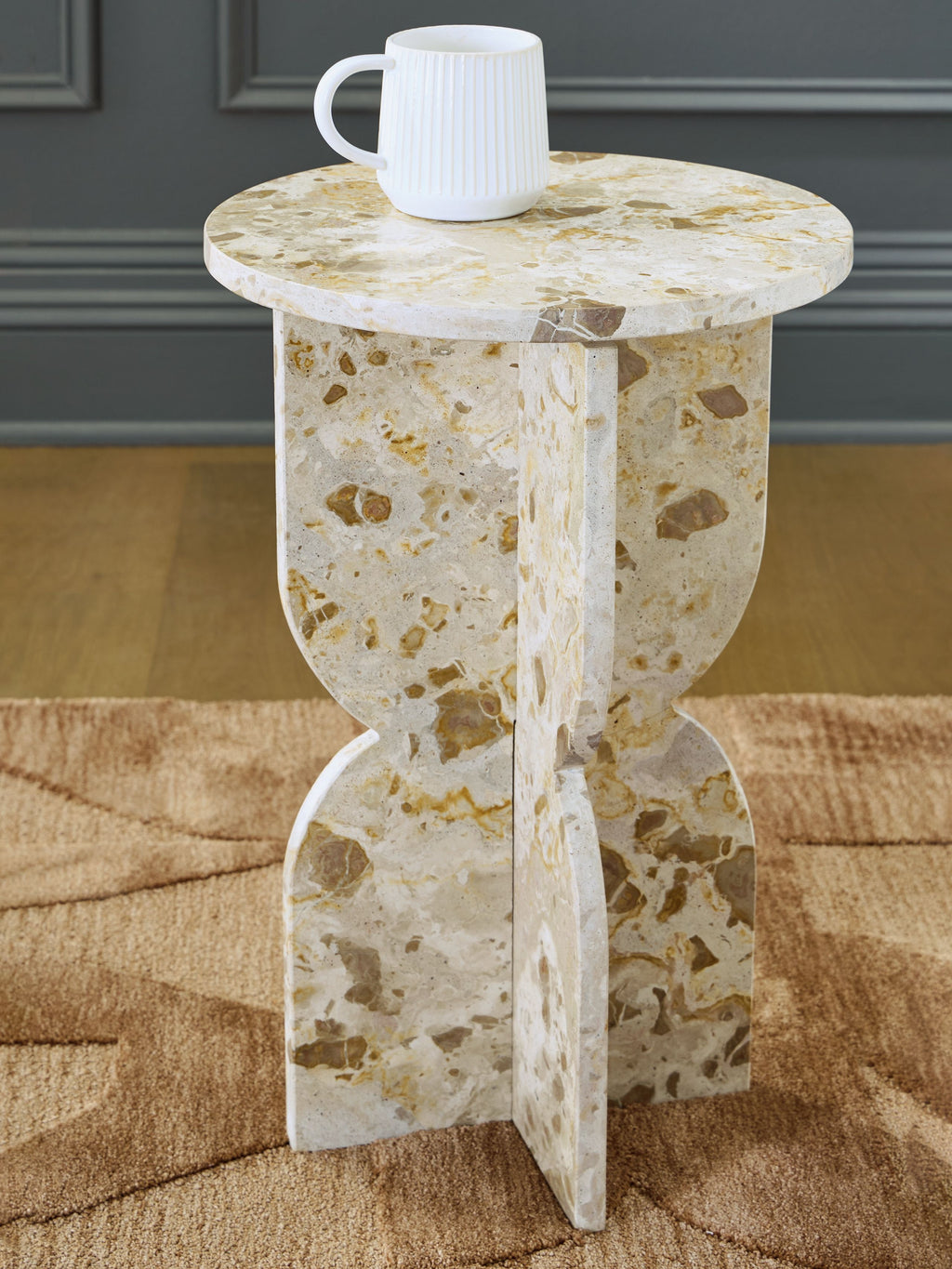 Beige stone-look accent table with round top and white mug on top