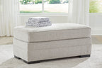 Light gray upholstered ottoman with cushioned top and black block feet