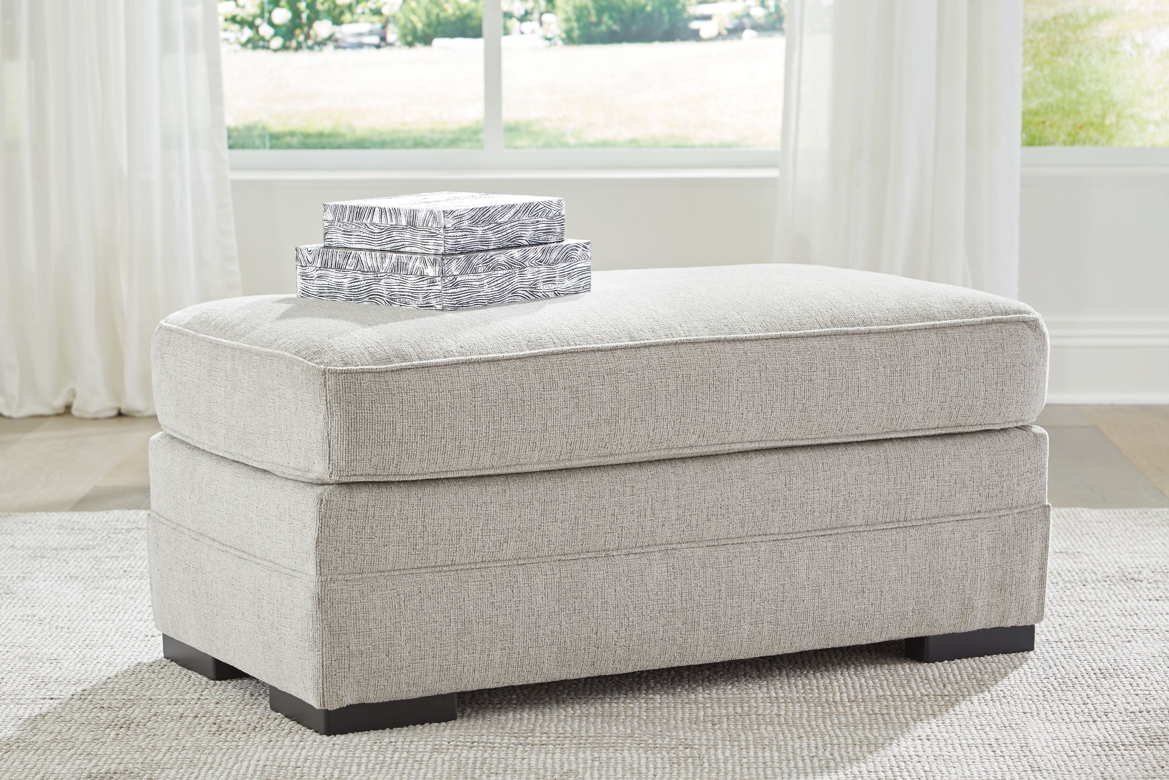 Light gray upholstered ottoman with cushioned top and black block feet