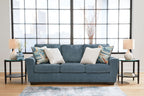 Blue upholstered sofa with three seat cushions and four pillows, including striped geometric throws