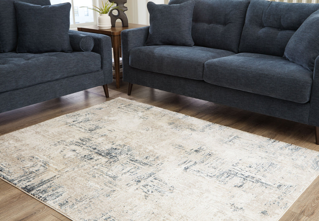 Cream abstract area rug with blue-gray distressed pattern beneath dark blue sofas.