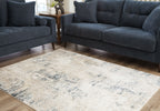 Cream abstract area rug with blue-gray distressed pattern beneath dark blue sofas.