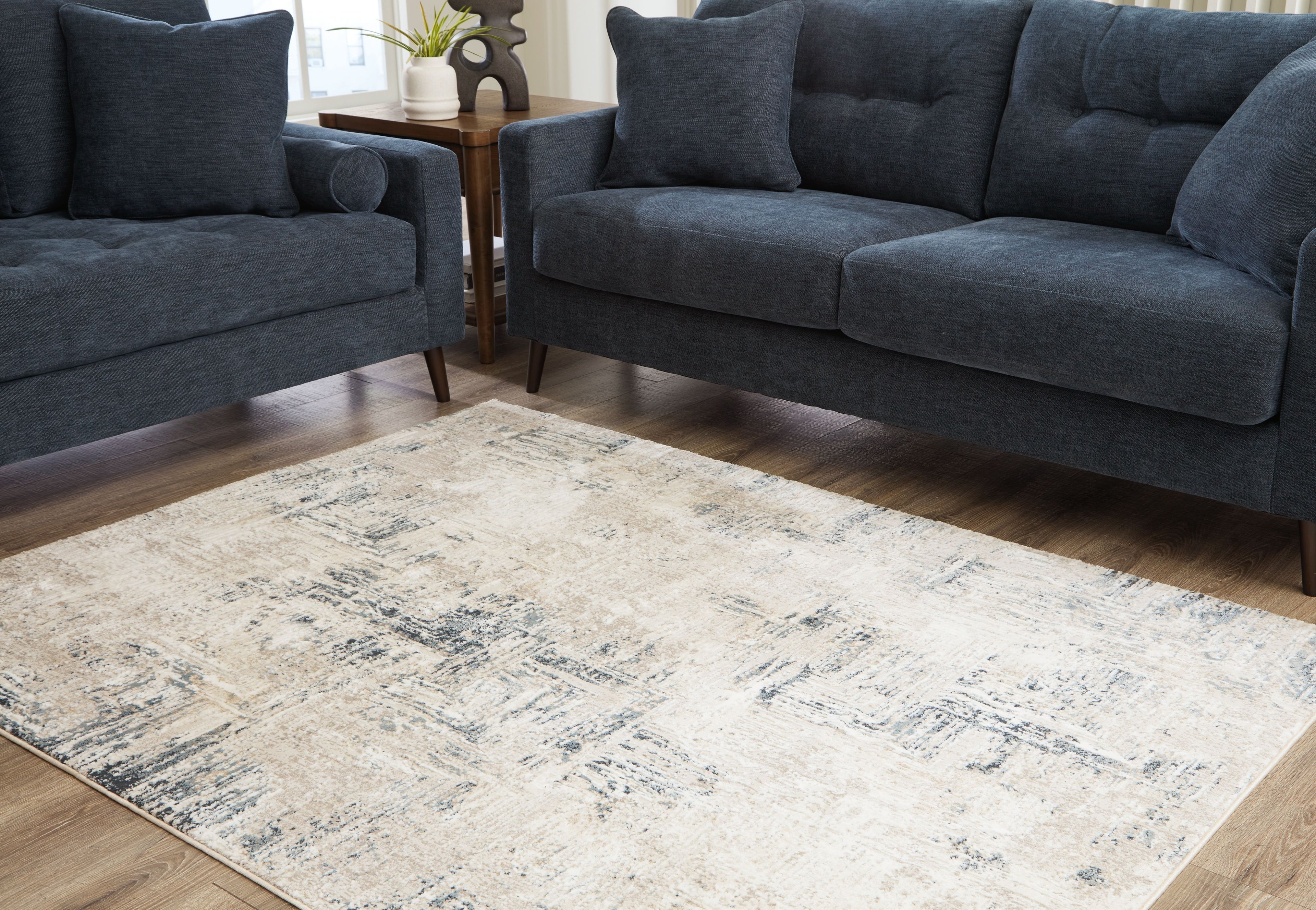 Cream abstract area rug with blue-gray distressed pattern beneath dark blue sofas.
