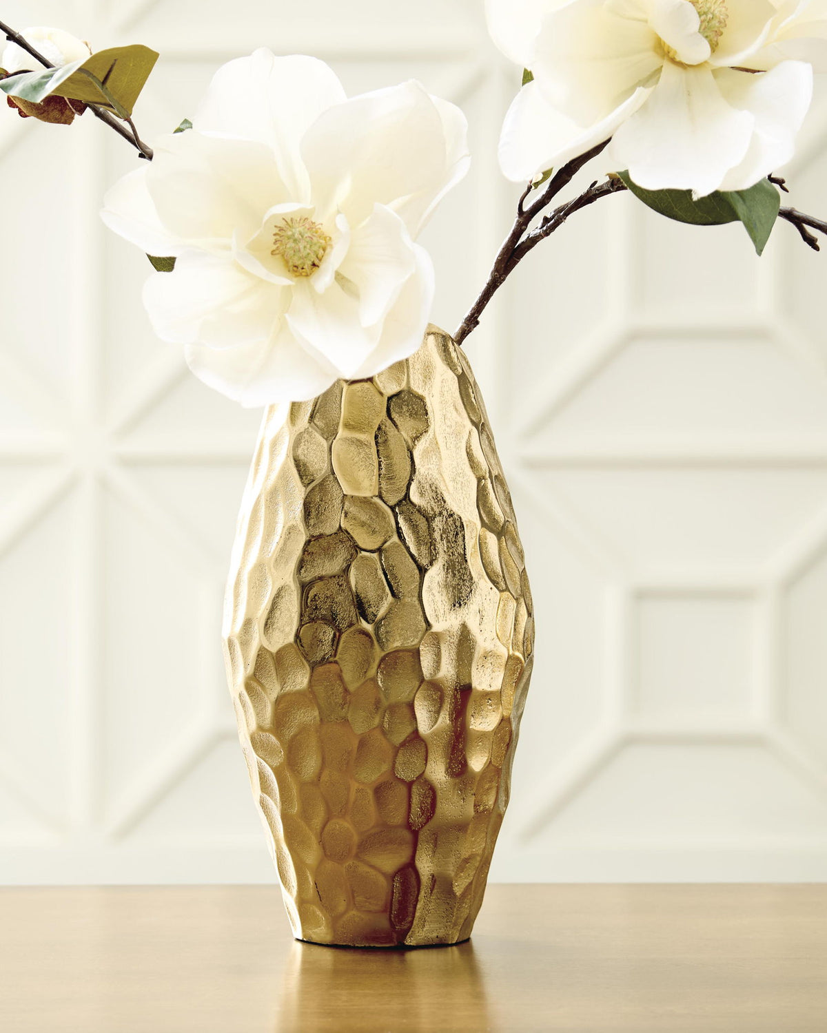 Gold hammered metal vase holding white flowers with green stems