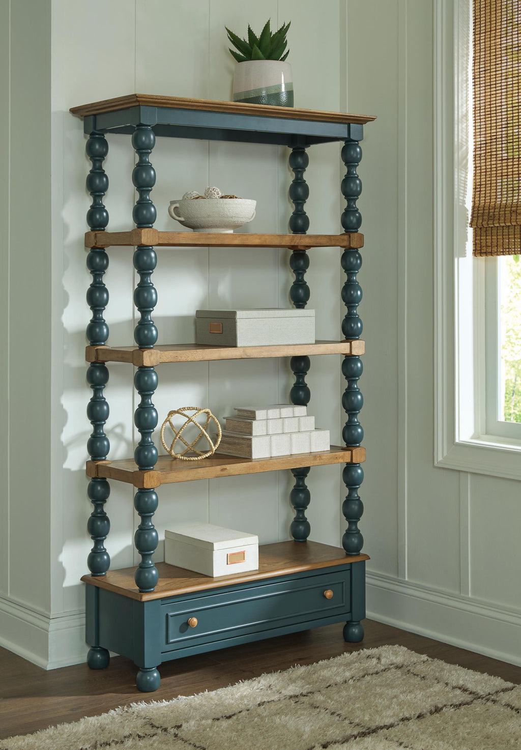 Blue bookcase with brown shelves and lower drawer, tall turned posts in an open frame.