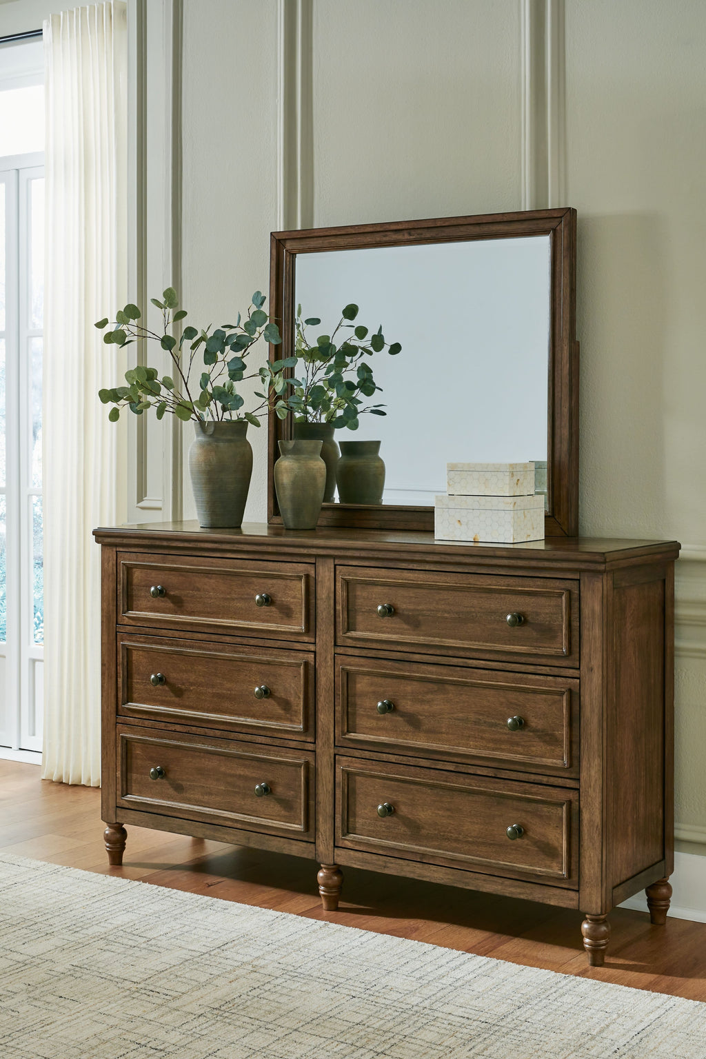 Brown wooden dresser with framed mirror above six drawers, decorative items on top