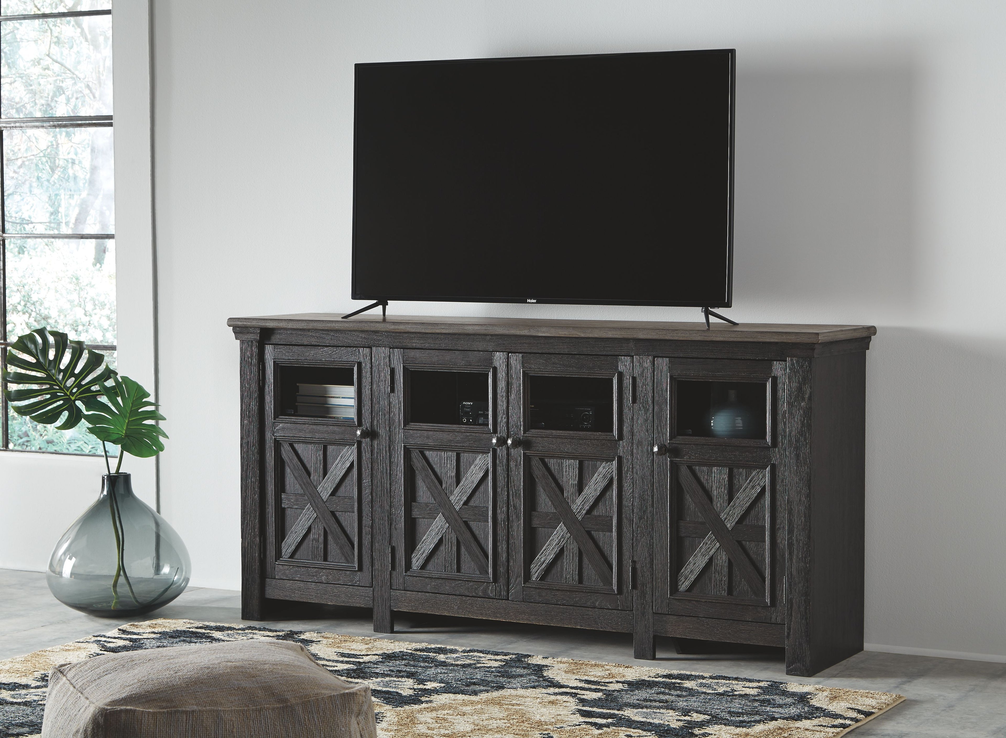 Black TV stand with gray tabletop and four X-pattern door panels; TV on top
