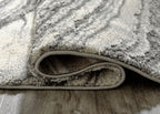 Rug corner close-up with folded edge and short textured pile in gray.