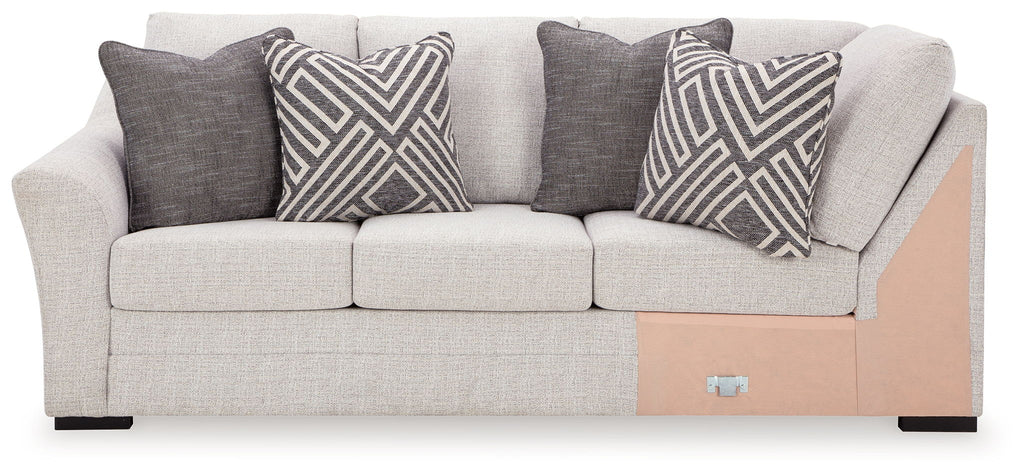 Stone-colored sofa with corner wedge, three seat cushions, and dark patterned throw pillows