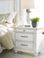 Whitewashed three-drawer nightstand with metal handles and turned legs, angled view