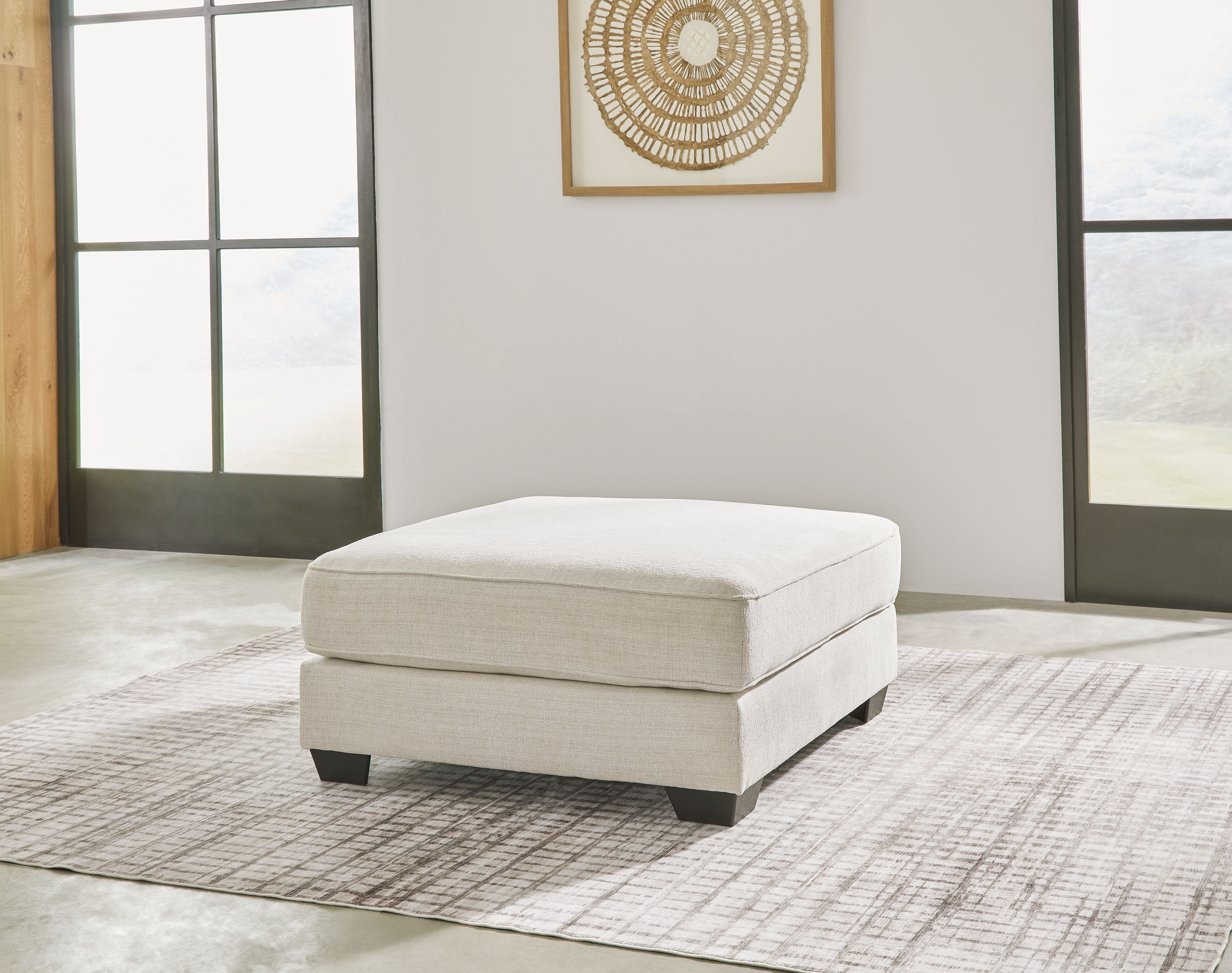 Oversized ottoman in beige fabric with black feet and a square cushion top.