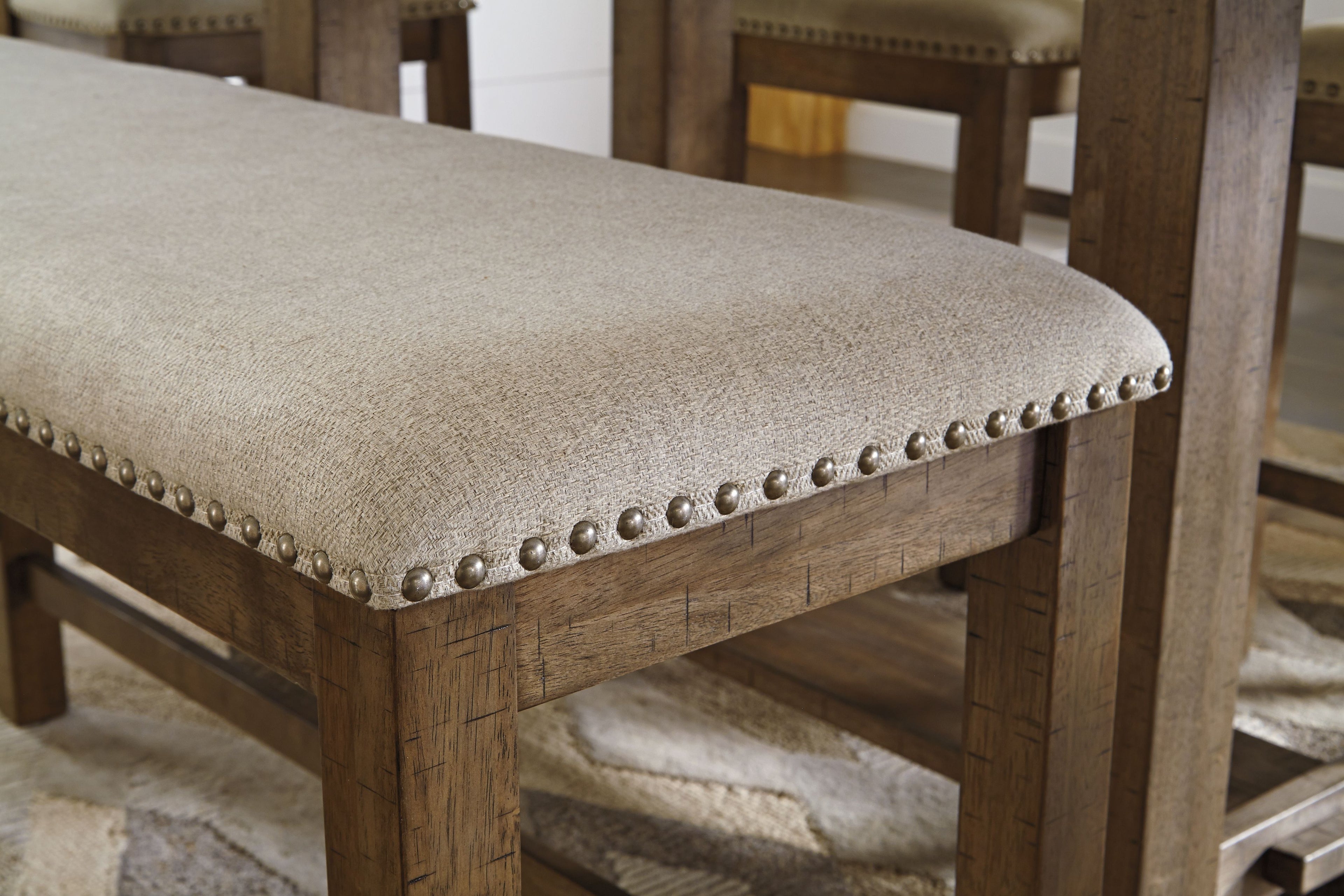 Beige upholstered bench seat with nailhead trim along the edges and dark wood frame