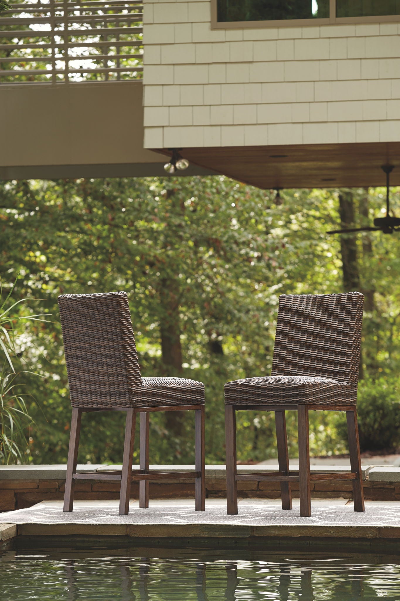 Outdoor woven barstools with dark brown frames near a stone deck