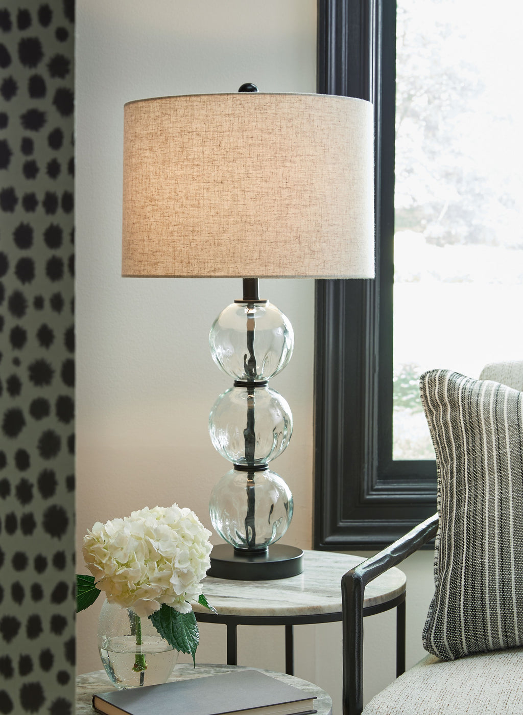 Glass table lamp with beige drum shade and clear stacked sphere base