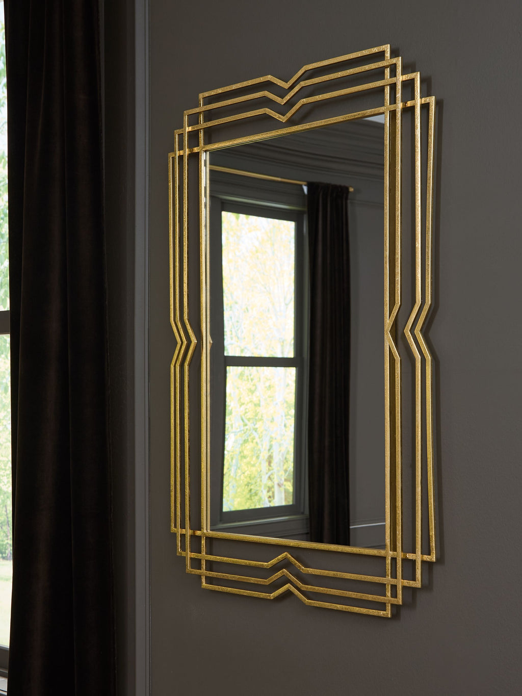 Gold accent mirror with layered geometric frame hung on a dark wall