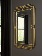 Gold accent mirror with layered geometric frame hung on a dark wall
