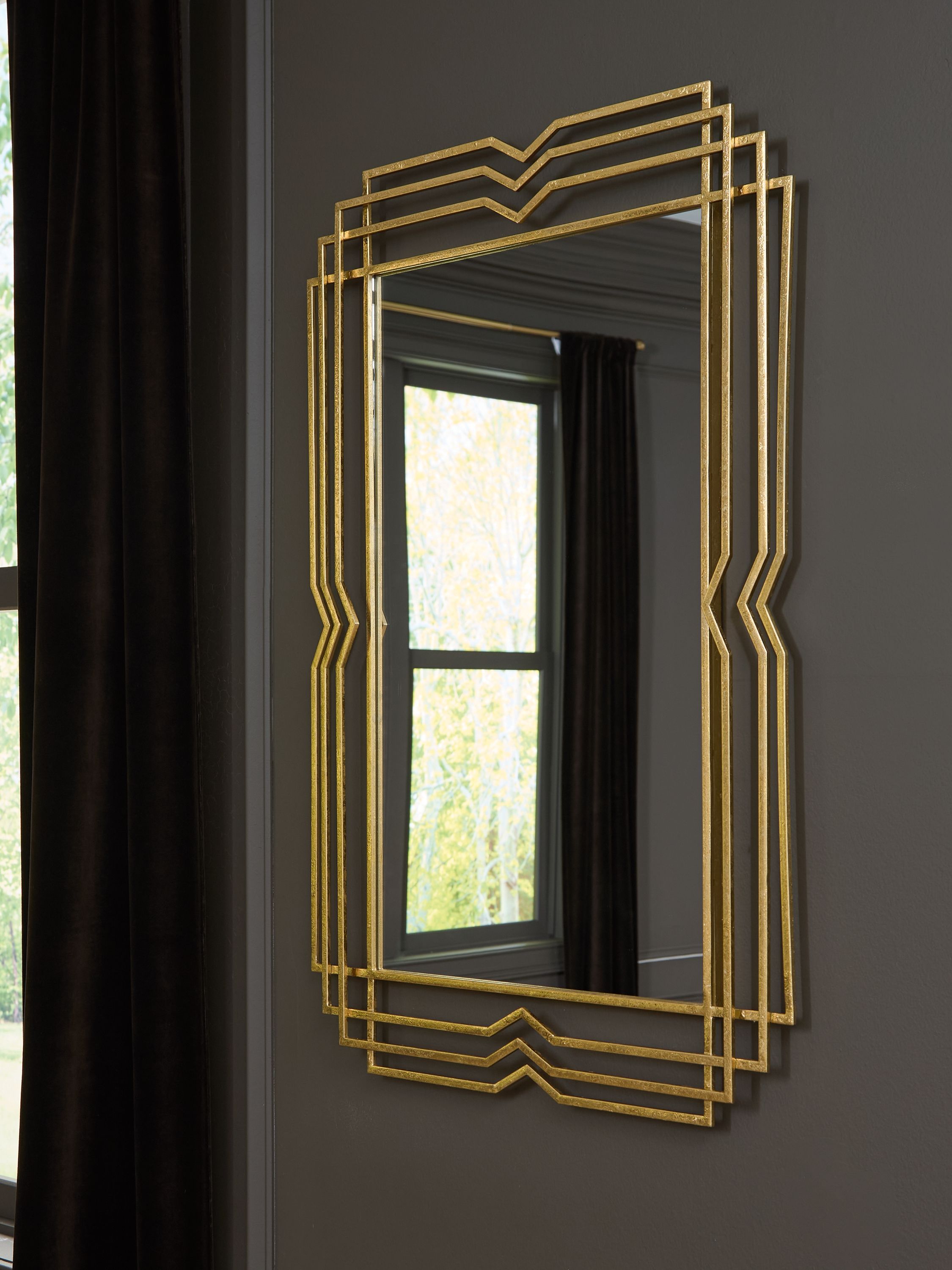 Gold accent mirror with layered geometric frame hung on a dark wall