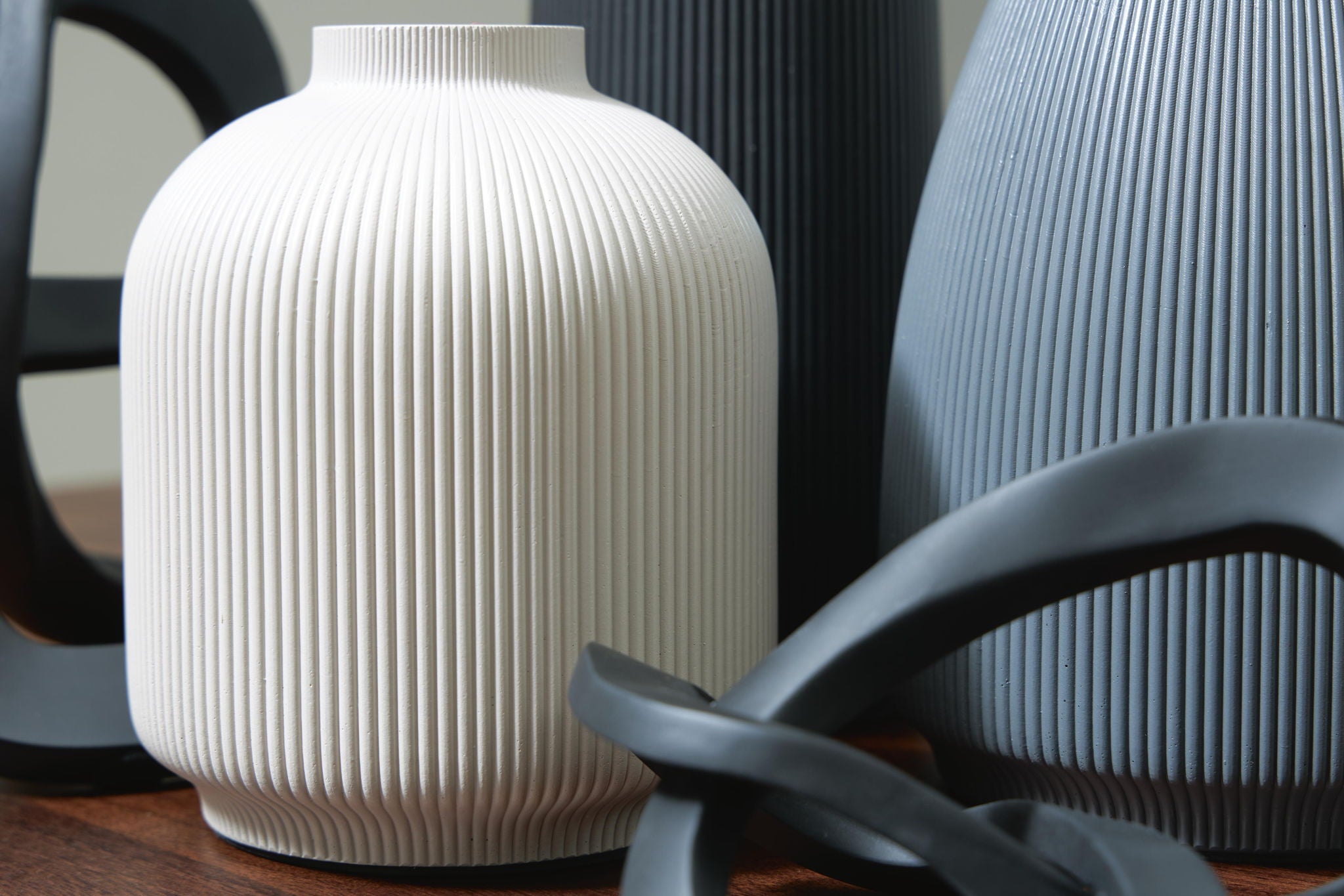 White ribbed ceramic vase with black loop accessory and neighboring gray vase
